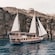 The Adonis luxury schooner sailing on the water near a cliff in Santorini, Greece
